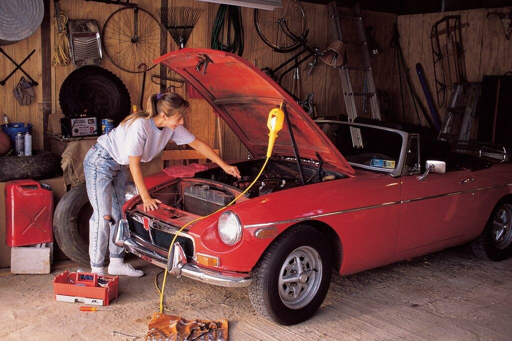 Woman looking under the hood of a red British sports car in a garage
