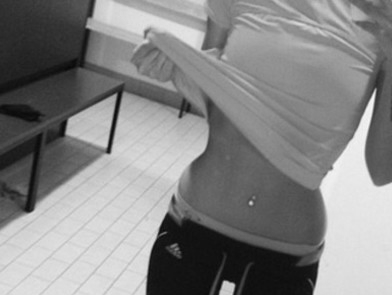 Female pulling up her shirt to show her contoured waist.