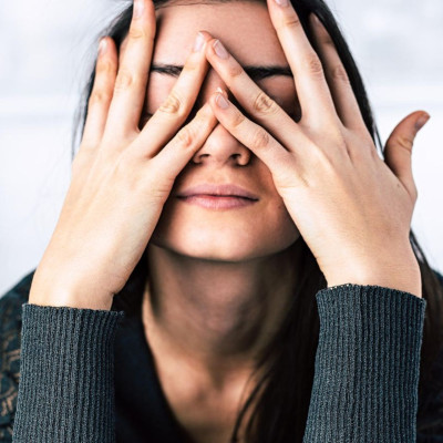 Woman sitting with elbows on table who appears stressed and has her hands partially covering her face