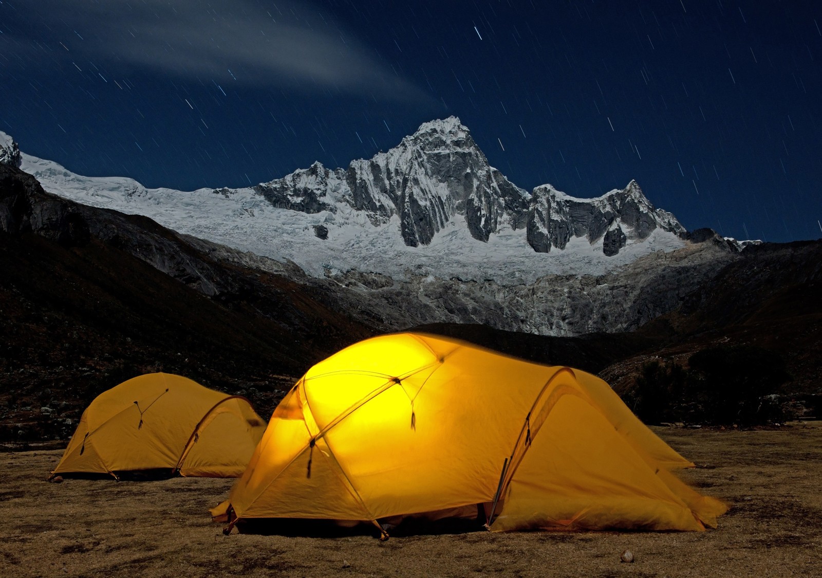 Two yellow tents popped in a mountain valley with mountain backdrop
