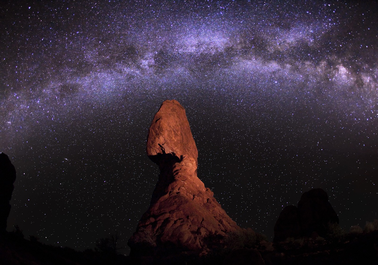 Giant rock formation in front of a starry night sky with purple hue