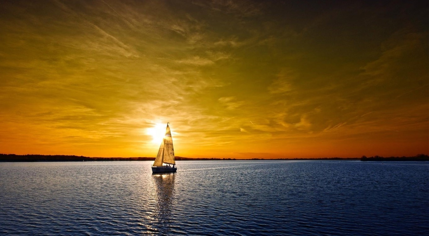 Sun halfway lit behind a saliing sailboat