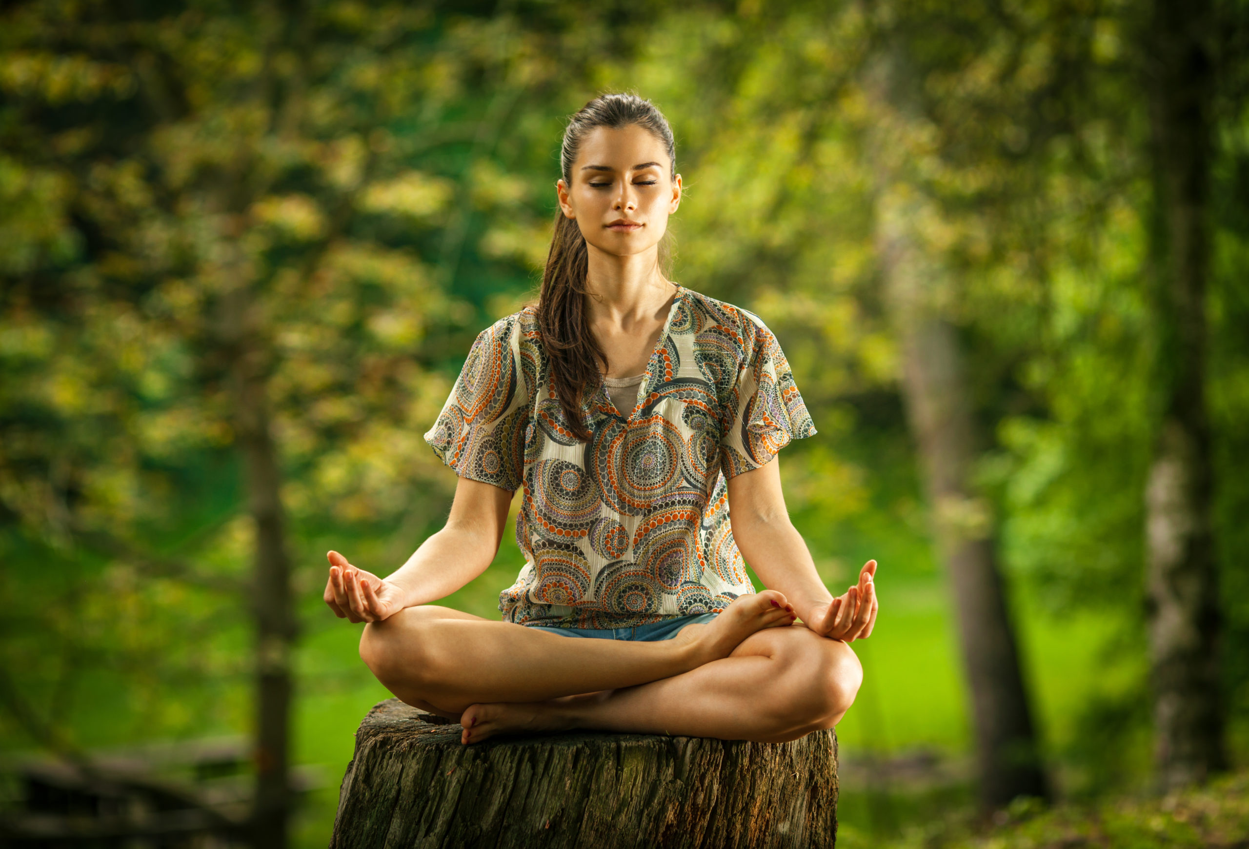 Female sitting cross-legged on a tree trunk meditating